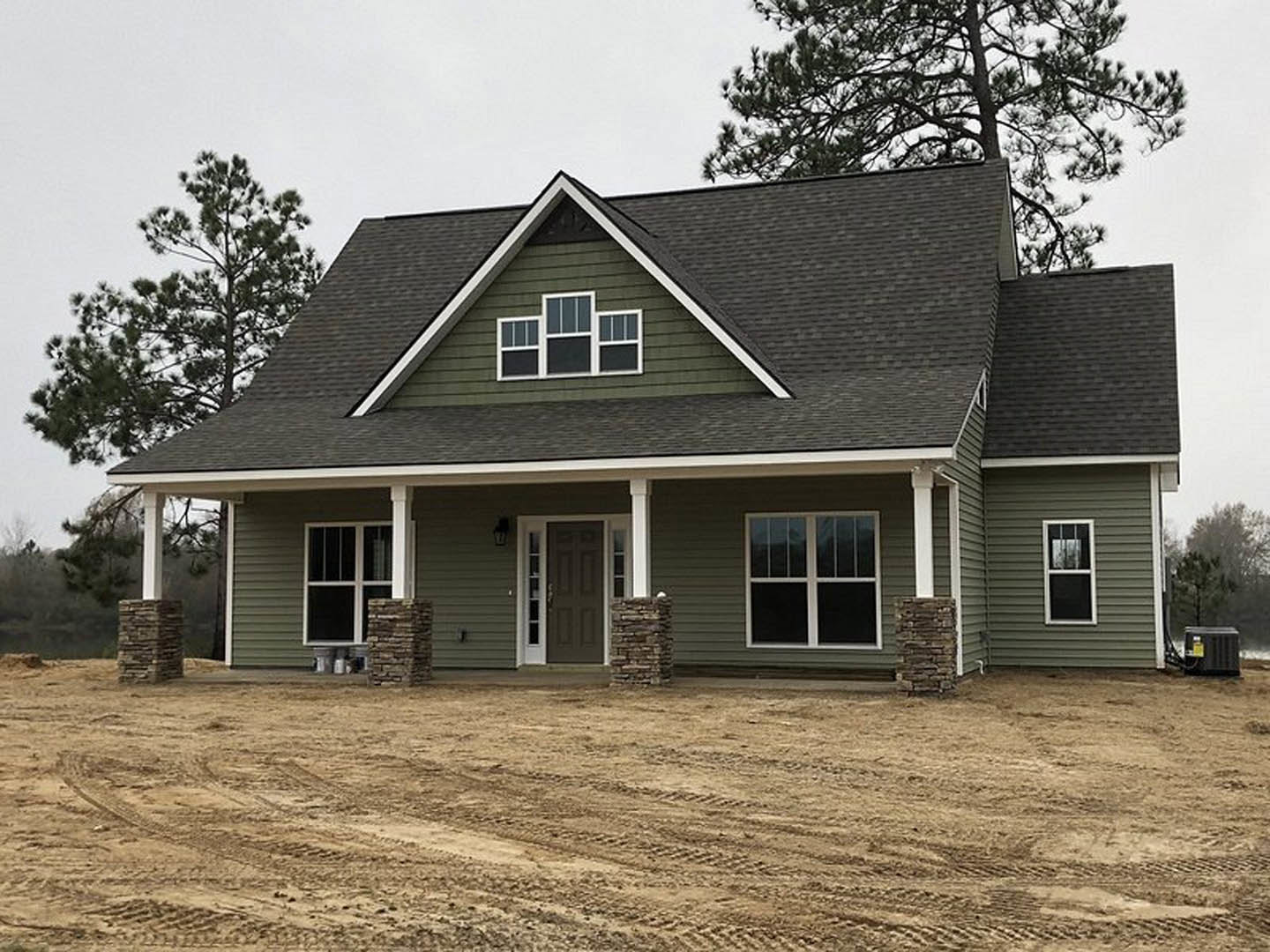 Green metal roof house with white-framed windows and door, dirt driveway with tire tracks, light siding, open sky above