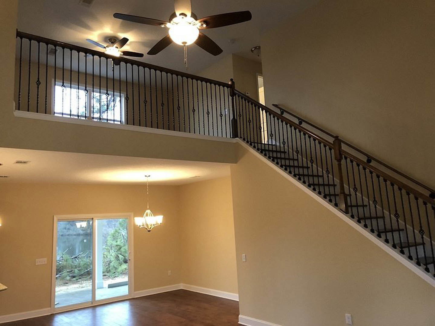 Open living area featuring a staircase with metal railings, ceiling fan with integrated light, sliding glass door overlooking a tree, and neutral walls with decorative molding