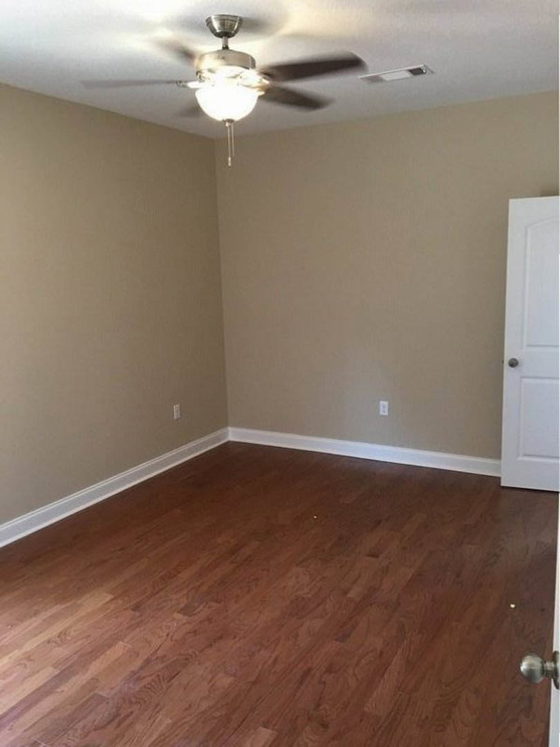 Living room with hardwood floors, white plaster walls, ceiling fan with light fixture, and a close-up view of a wooden door and metal door knob