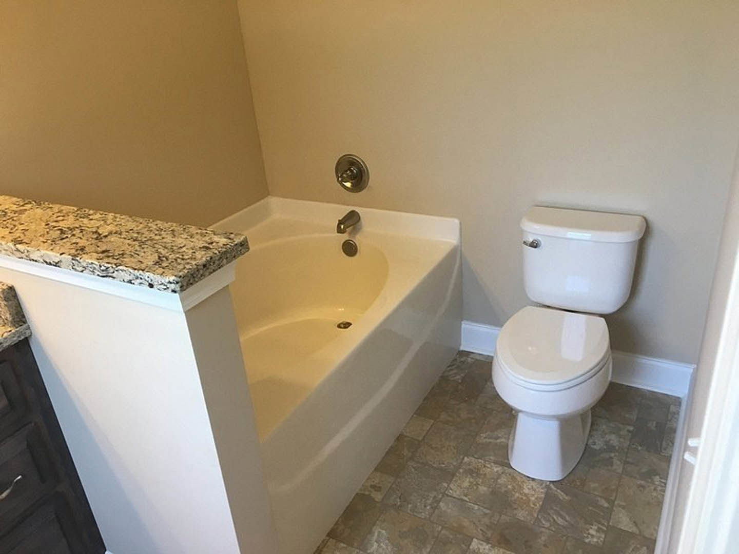 Bathroom with white toilet, closed seat, silver handle, white bathtub, chrome faucet, light-colored countertop, tile walls, and brushed metal door knob
