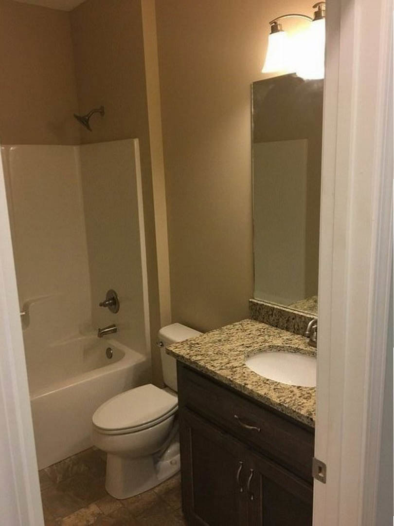 Modern bathroom with white porcelain sink and toilet, chrome faucet, tiled walls, and light-colored countertop with round vessel sink.