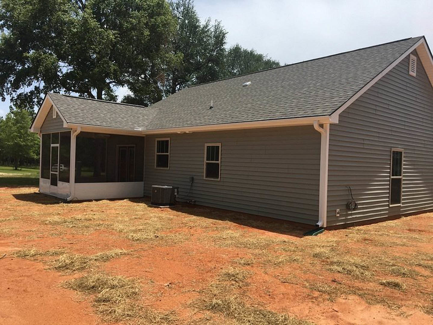 Two-story house with white columns, large windows with white frames, black mailbox near entry, surrounded by green lawn and mature trees