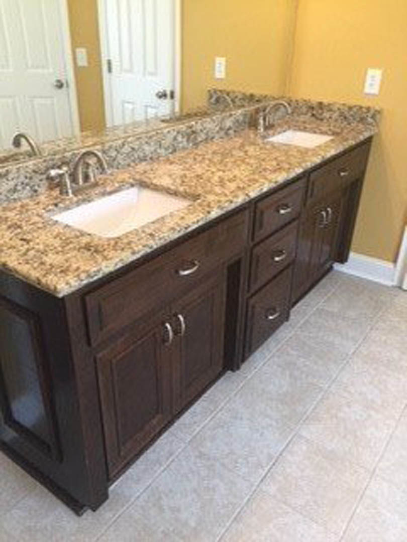 Modern bathroom with two undermount sinks set in a quartz countertop, white cabinetry below, large frameless mirror above, chrome faucets, and light gray tile backsplash