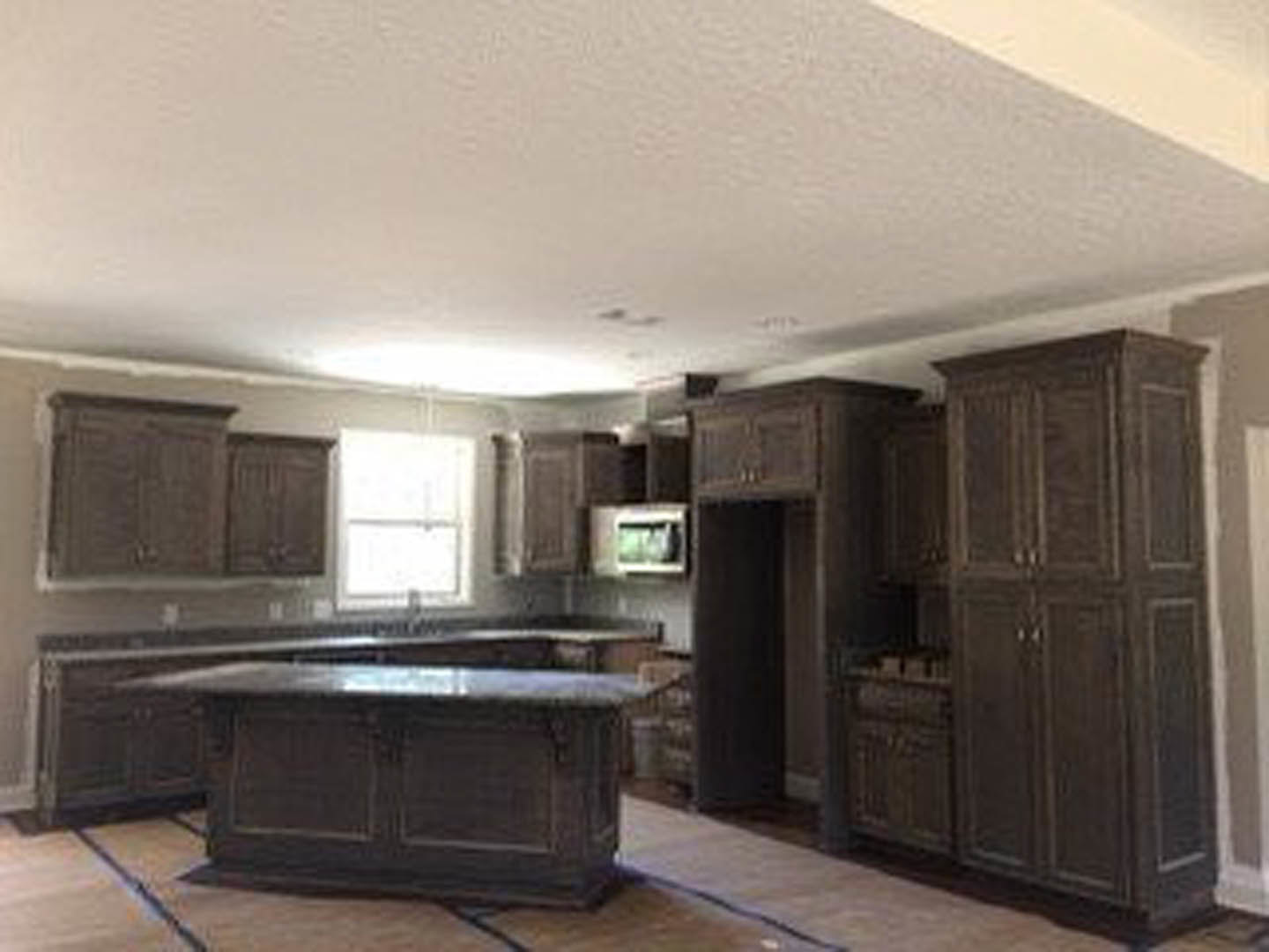Spacious kitchen featuring a large central island with light countertops, black cabinetry, wood flooring, and a white-framed window providing natural light.