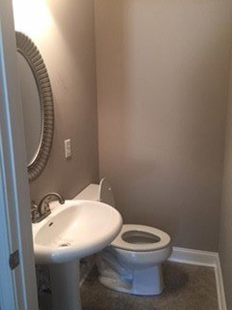 White porcelain sink with chrome faucet beside a toilet, both set against light tiled walls; mirror above sink and plastic bag covering toilet seat.
