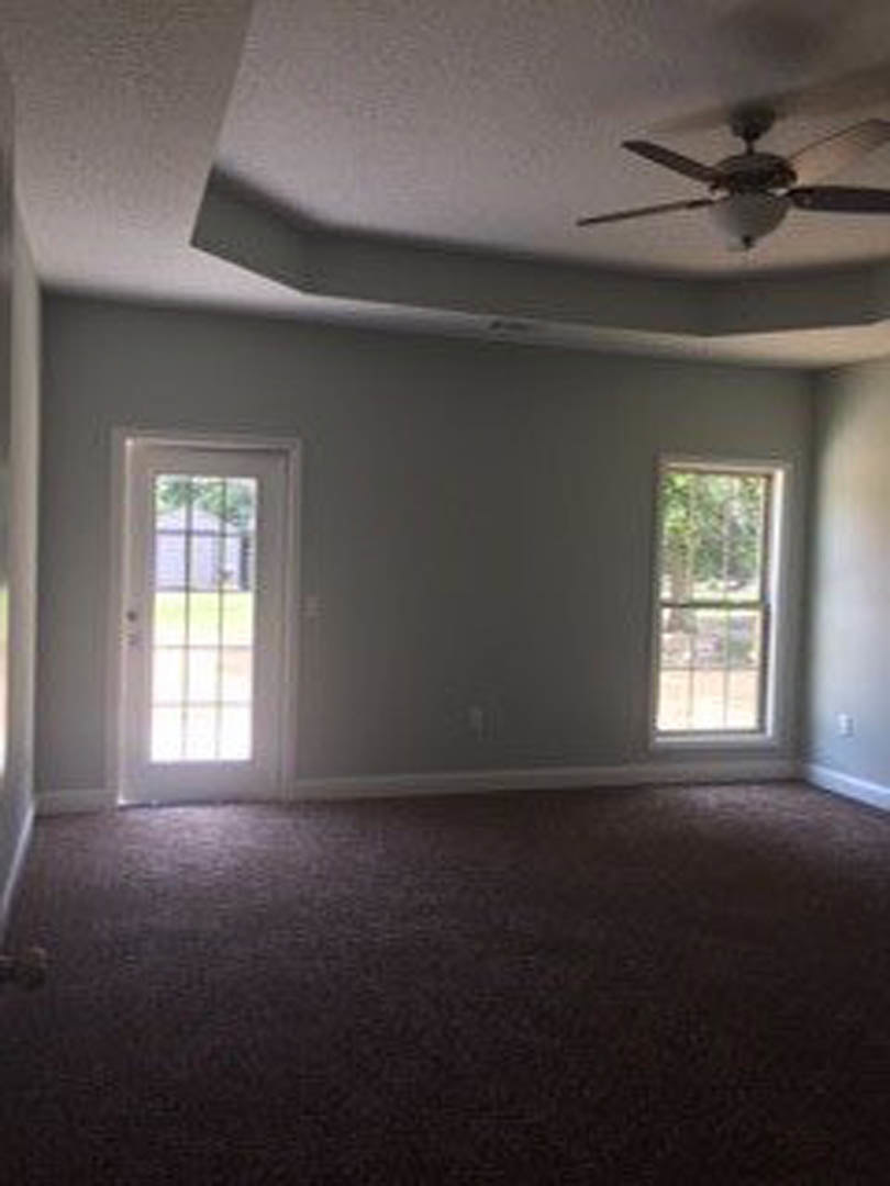 Ceiling fan with light fixture mounted on white ceiling, two white doors—one with glass panes—dark carpeted floor, window overlooking trees, neutral walls.