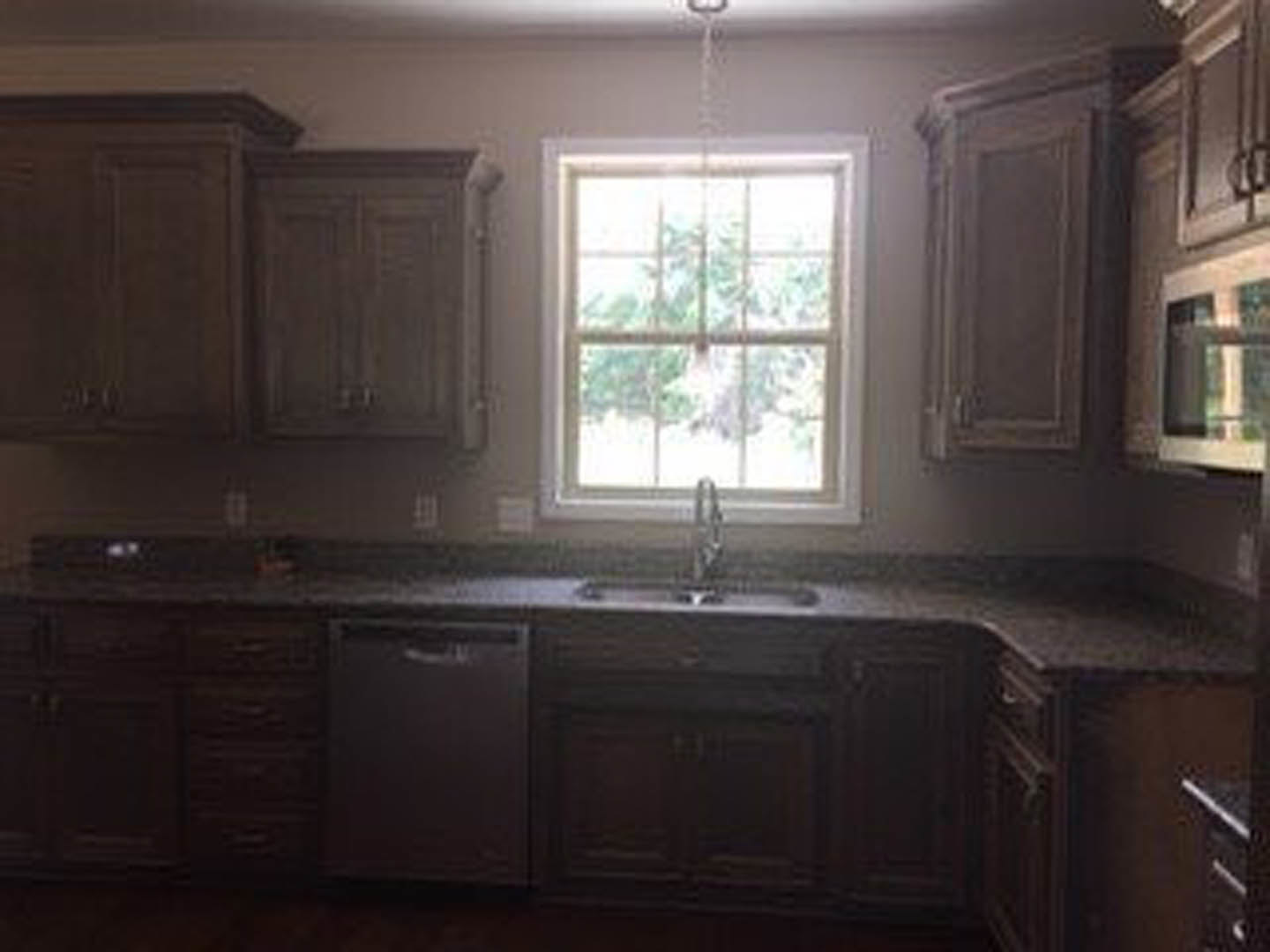 Modern kitchen featuring white cabinetry, quartz countertops, stainless steel sink beneath a large window, and natural light illuminating the space.