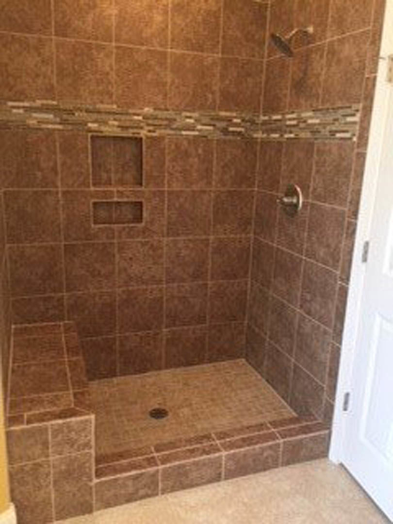 Walk-in shower with brown tile walls, white door, metal drain, and marble tile flooring