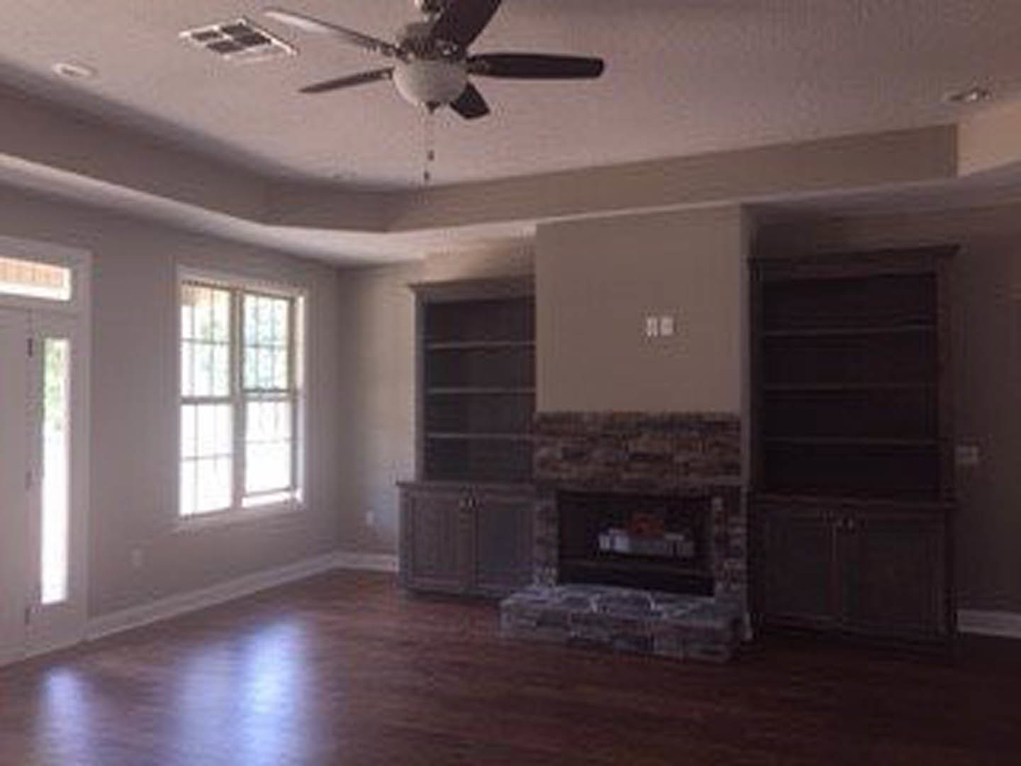 Living room with stone fireplace, wood mantel, ceiling fan, neutral walls, and hardwood flooring