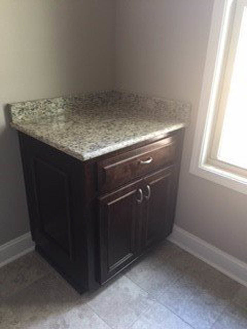 Granite countertop in kitchen corner with black cabinetry, white wall, and stainless steel sink