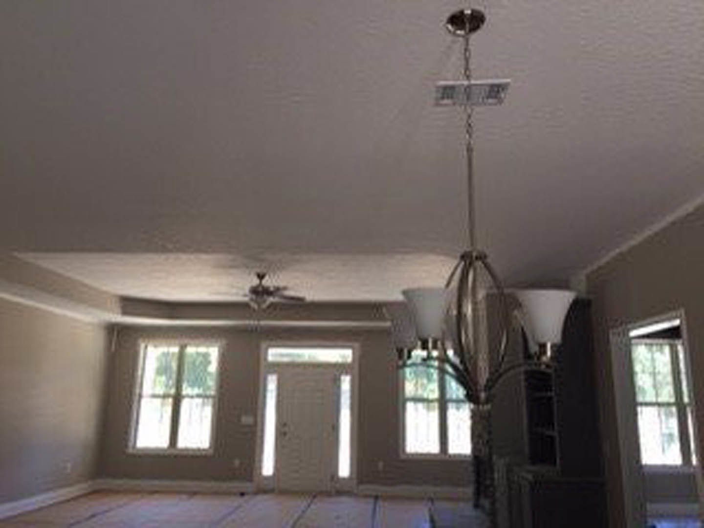 Living room with white plaster walls, ceiling fan, chandelier, wood flooring, large window with white trim, and white paneled door
