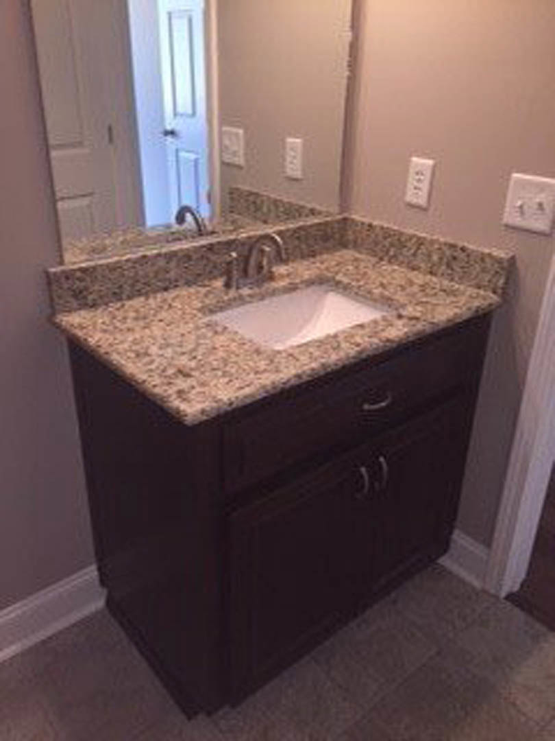 White porcelain sink with chrome faucet set in brown wood vanity, light stone countertop, tiled floor, and neutral wall in modern bathroom.