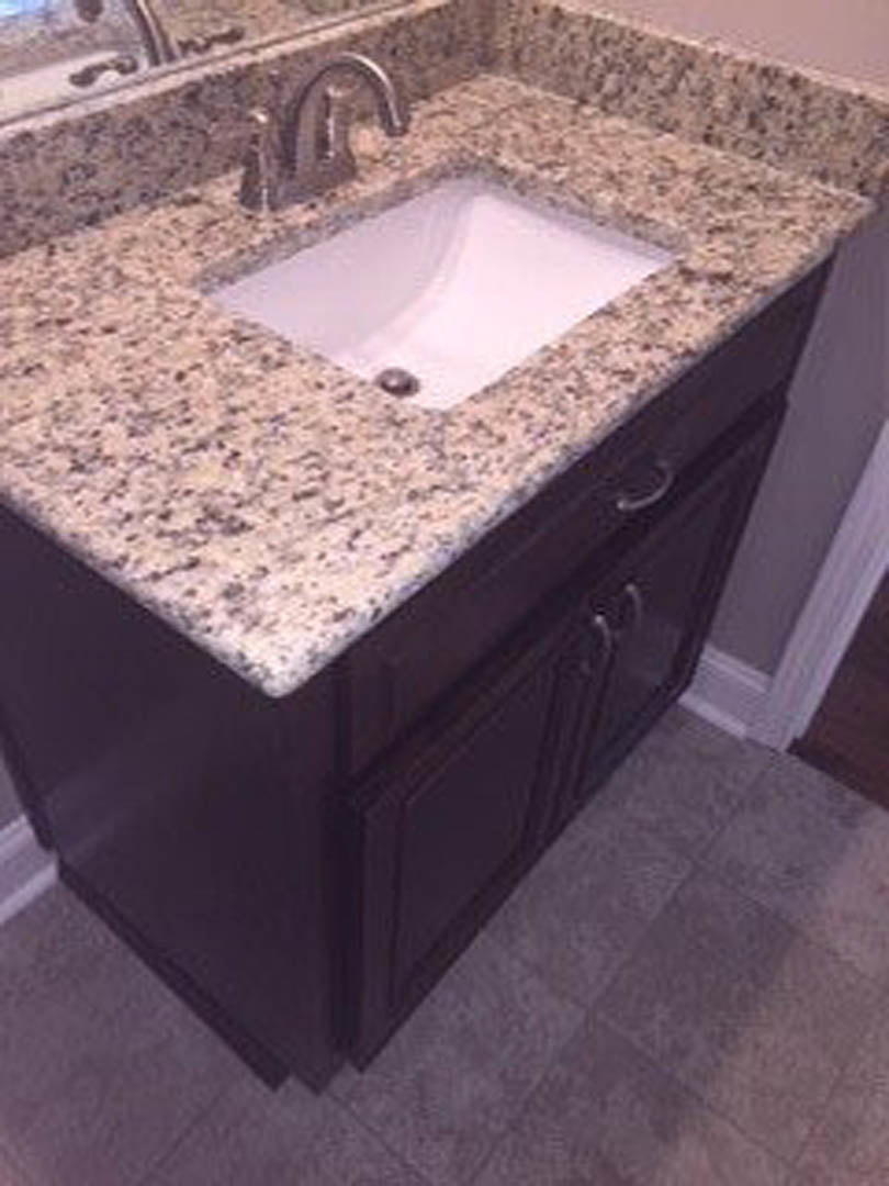 White porcelain undermount sink set in granite countertop with chrome faucet, surrounded by beige tile backsplash and bathroom accessories