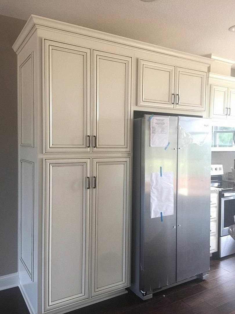 White kitchen cabinets, stainless steel refrigerator with a paper taped to the door, white interior doors with silver handles, white cloth with red mark on countertop.