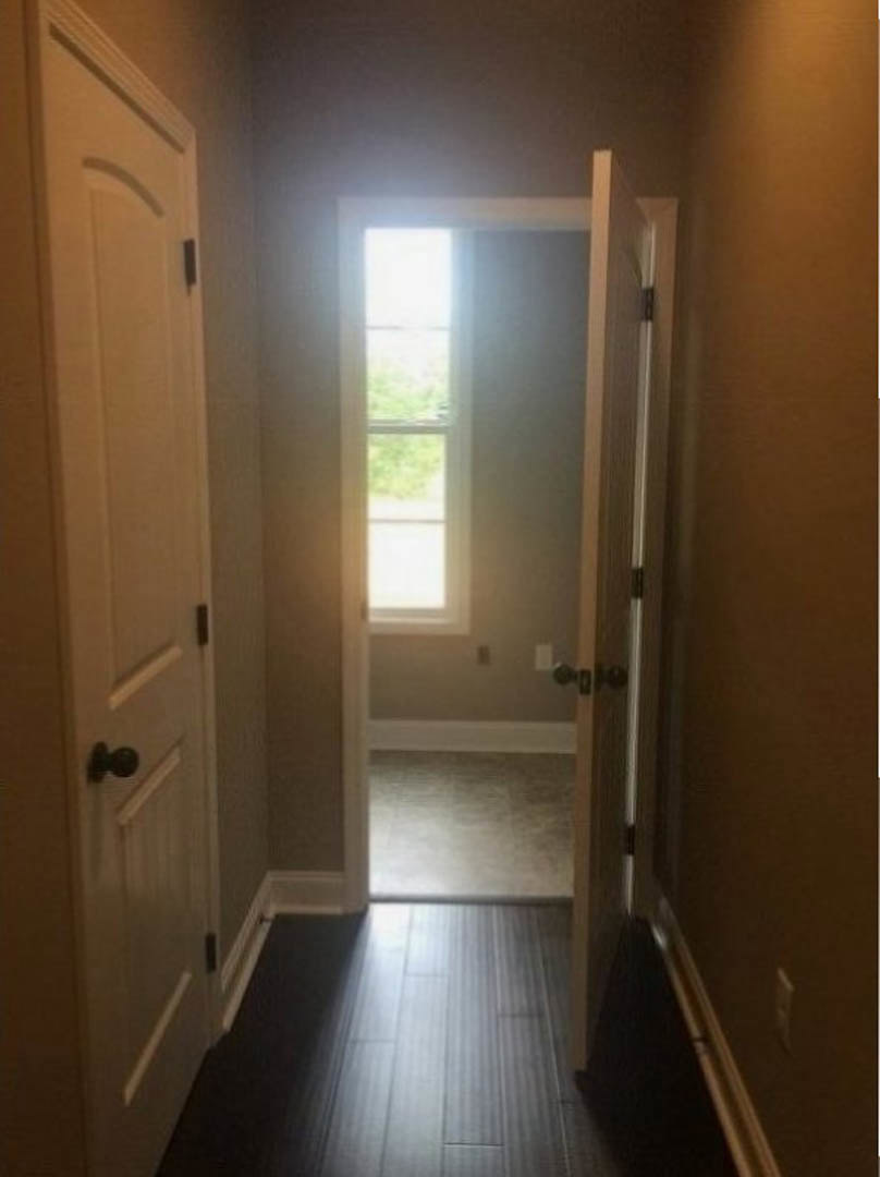 Hallway with dark wood flooring, open door featuring a window, light illuminating the floor, white walls, and modern door handle