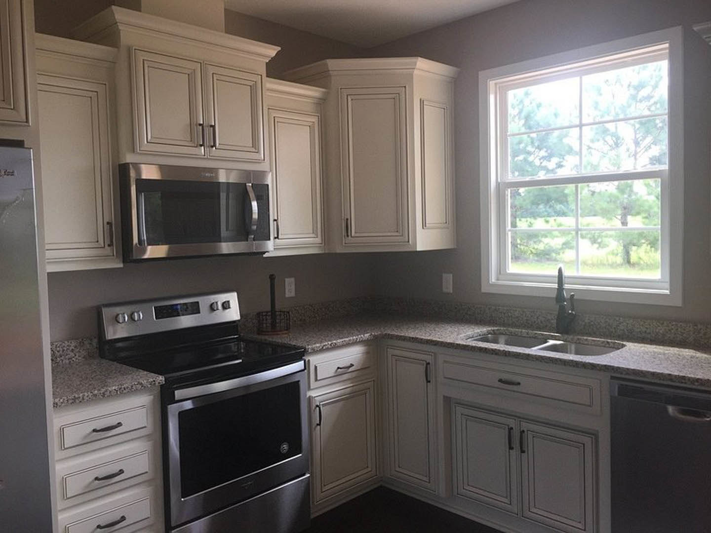 White kitchen with granite countertops, stainless steel stove and microwave, multi-pane window, white cabinetry, and white trim along walls and floor.