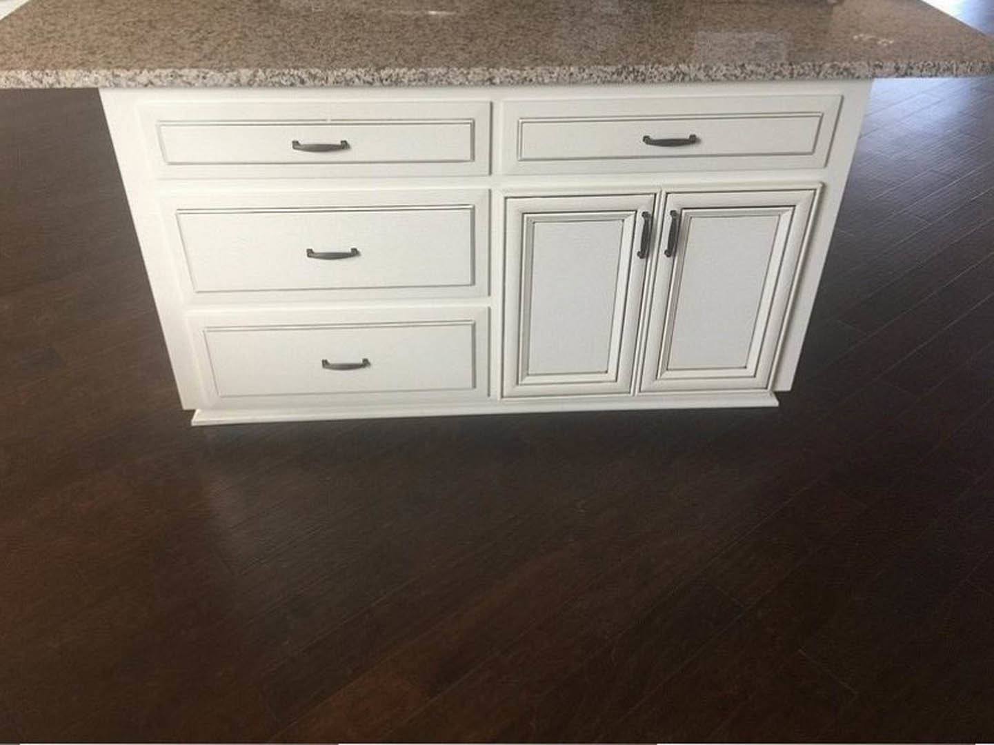 White kitchen island with marble countertop, white cabinetry featuring black handles, hardwood flooring, and close-up of drawers.