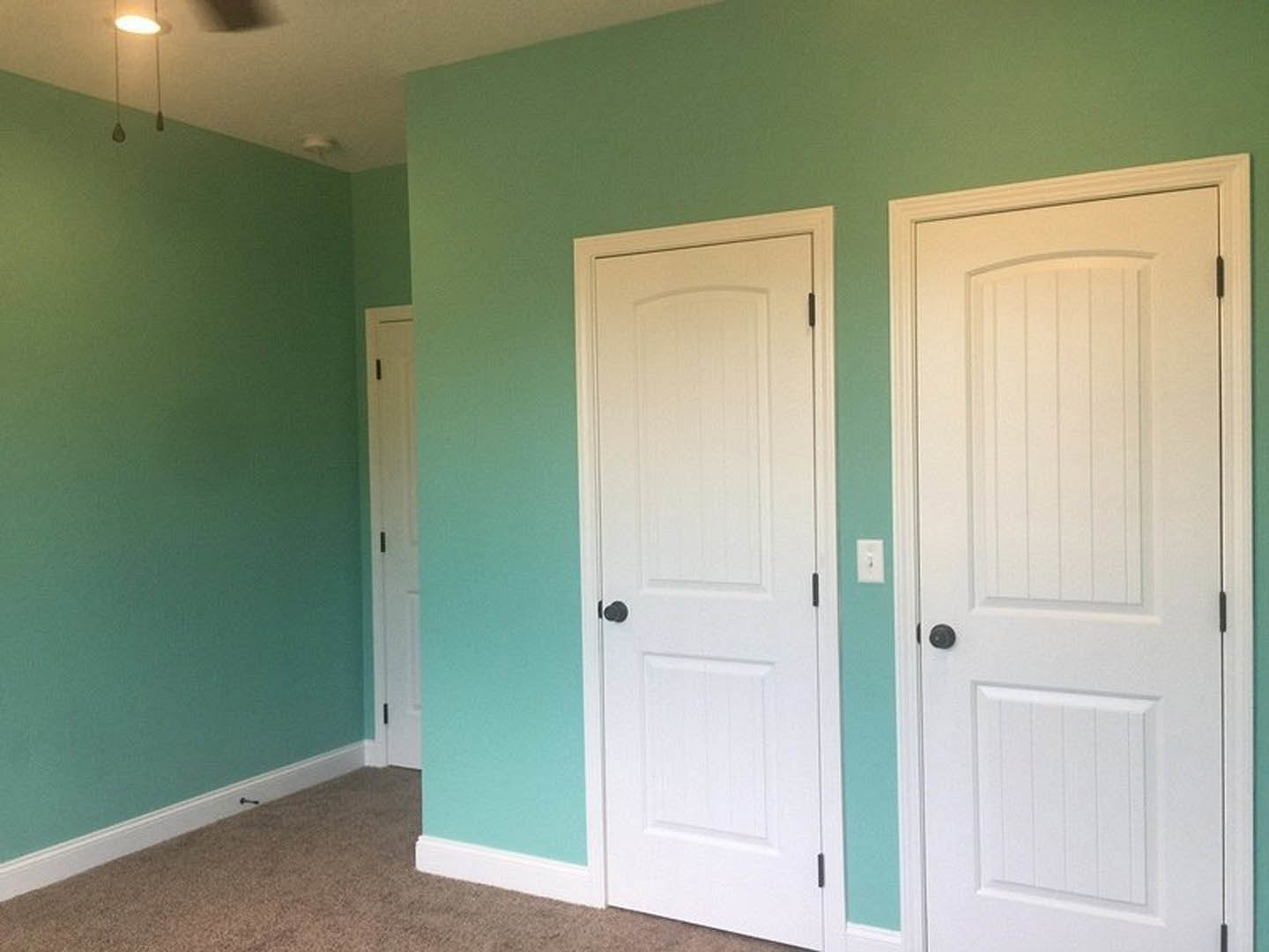 Two white doors with black handles in a room featuring white tile walls and light fixture