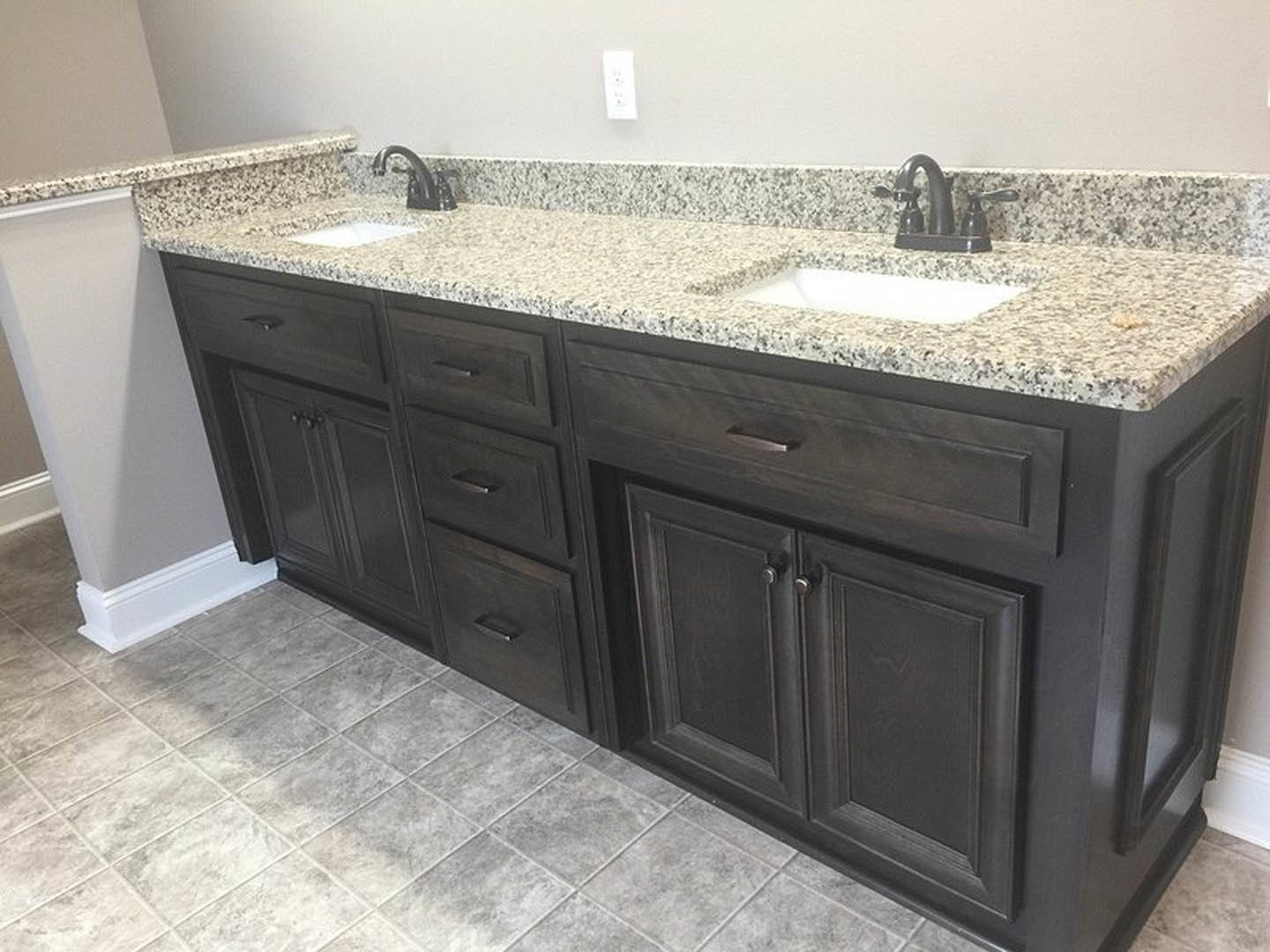 Granite bathroom countertop with undermount sink, chrome faucet, white cabinetry, and tile backsplash