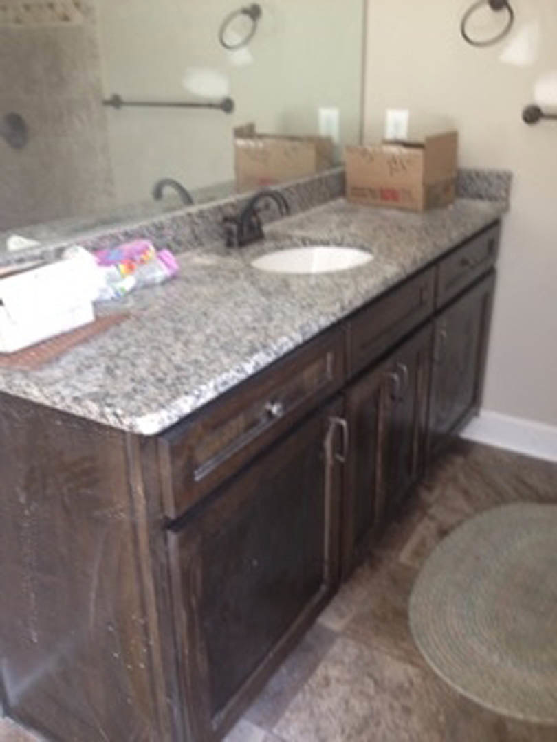 Modern bathroom featuring a granite countertop with an undermount sink, chrome faucet, large framed mirror, white tile backsplash, and light wood cabinetry with drawers.