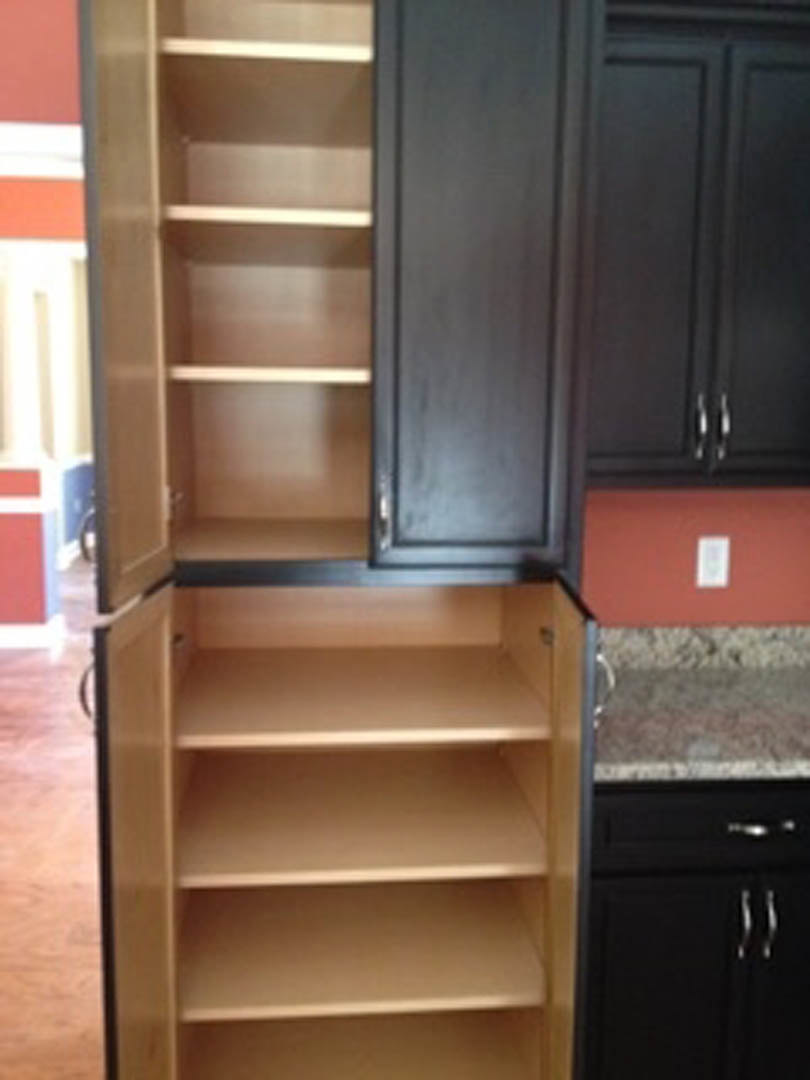 Black cabinet with open shelving, matte finish, white rectangular object and light switch mounted on deep red wall, close-up of grey and black doors, plywood shelf inside cabinet.