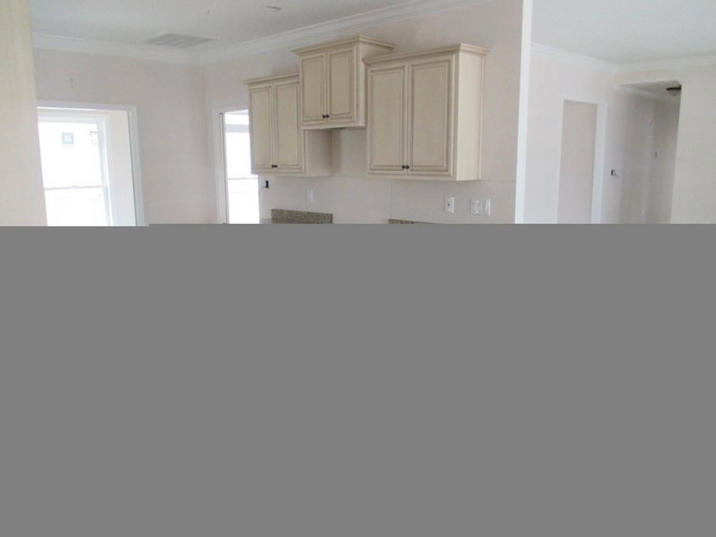White kitchen with shaker cabinets, quartz countertops, stainless steel sink, white tile backsplash, and sunlight streaming through a window and door.