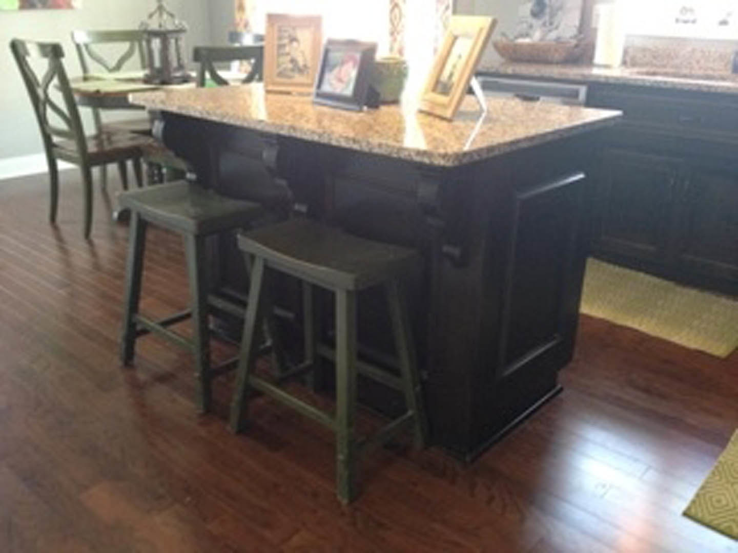 Kitchen island with wood stools, framed artwork on wall, light wood flooring, neutral cabinetry, blurred figure in background