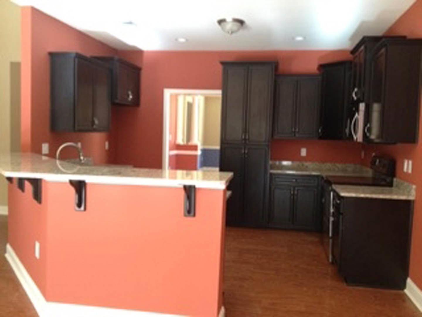 Black kitchen cabinets with brushed metal handles, white quartz countertop, stainless steel sink, light wood flooring, and neutral painted walls
