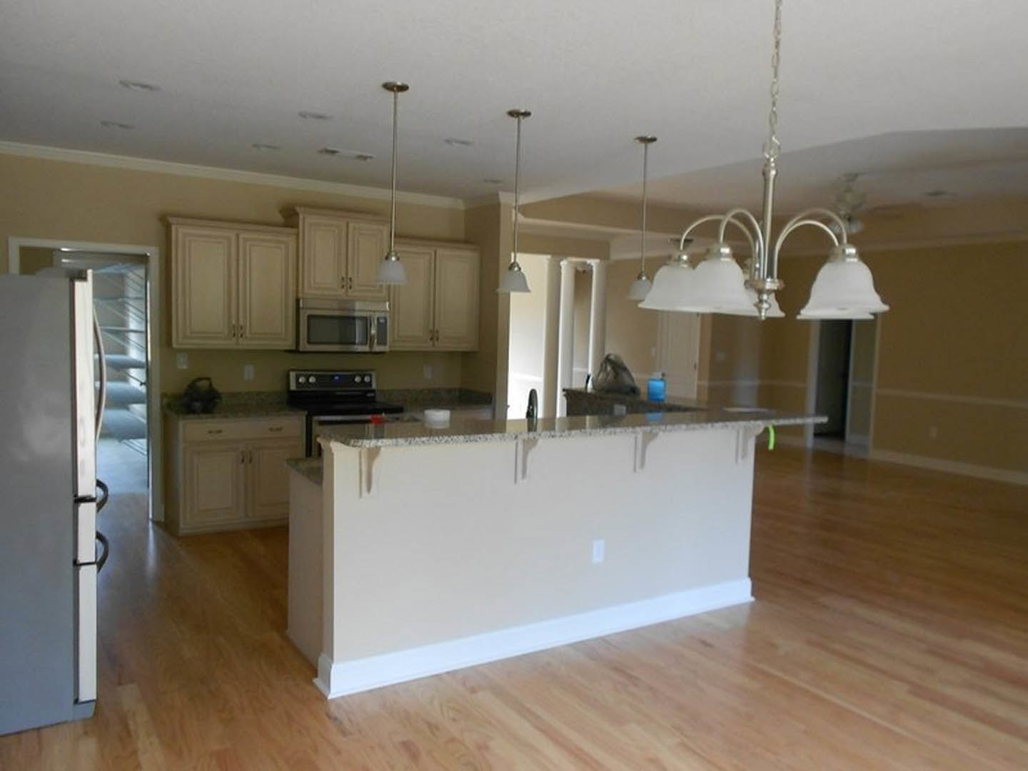 Open-concept kitchen and dining area with wood flooring, white cabinetry, stainless steel appliances including refrigerator and stove, stone countertops, and a modern chandelier