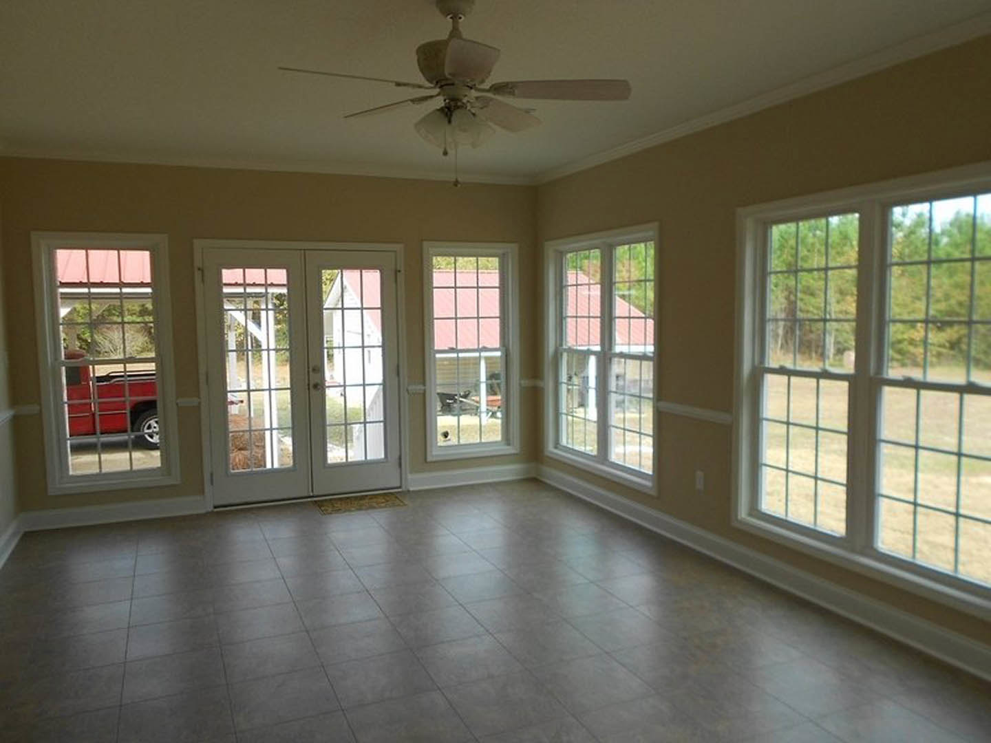 Ceiling fan with light fixture, multi-pane windows, tile flooring, double glass doors, red truck visible outside window