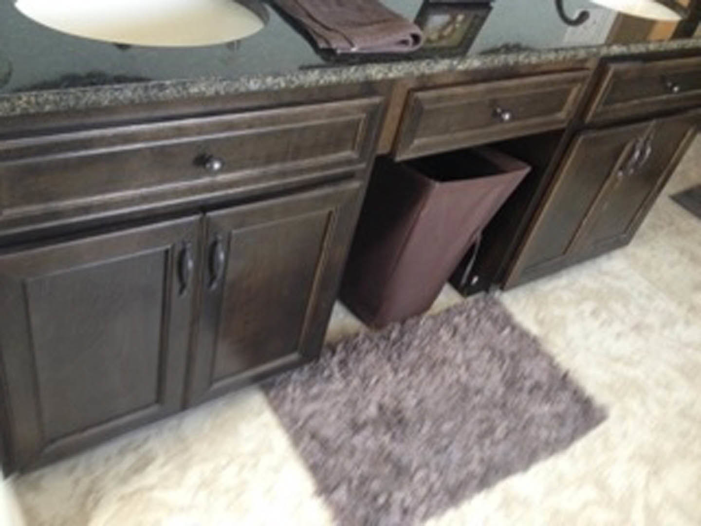 White bathroom sink with chrome faucet, light wood vanity, woven basket and trash can underneath, tile flooring