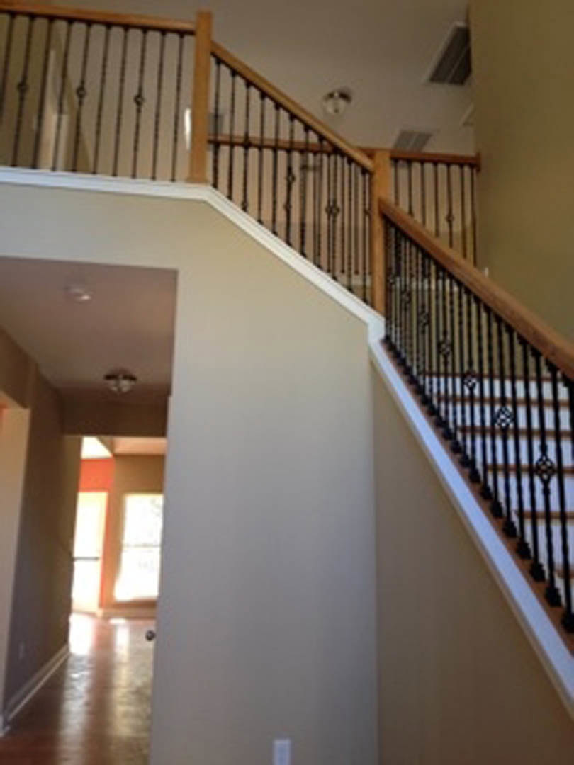 Modern staircase with black metal railings, light wood steps, and white walls in a bright hallway