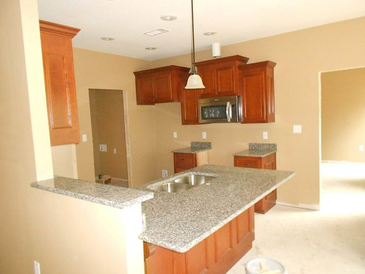Granite countertops, wood cabinetry, stainless steel sink, built-in microwave, tile backsplash, light switch on wall