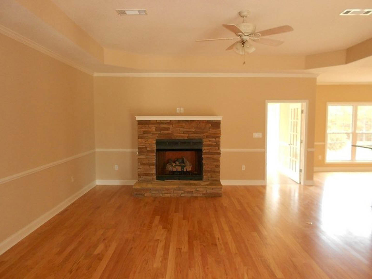 Living room with brick fireplace, hardwood floors, ceiling fan, white door, and molding details