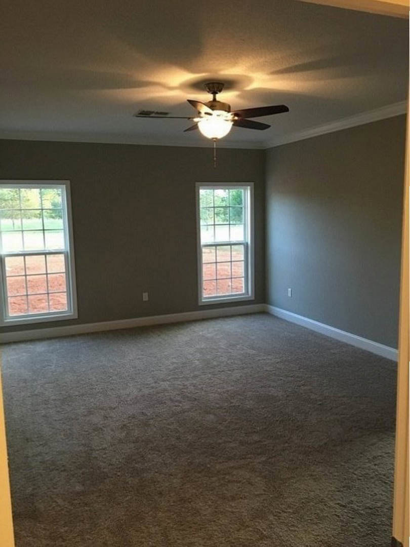 Bright room with two large windows featuring multiple square panes, ceiling fan with integrated light fixture, neutral plaster walls, and light wood flooring