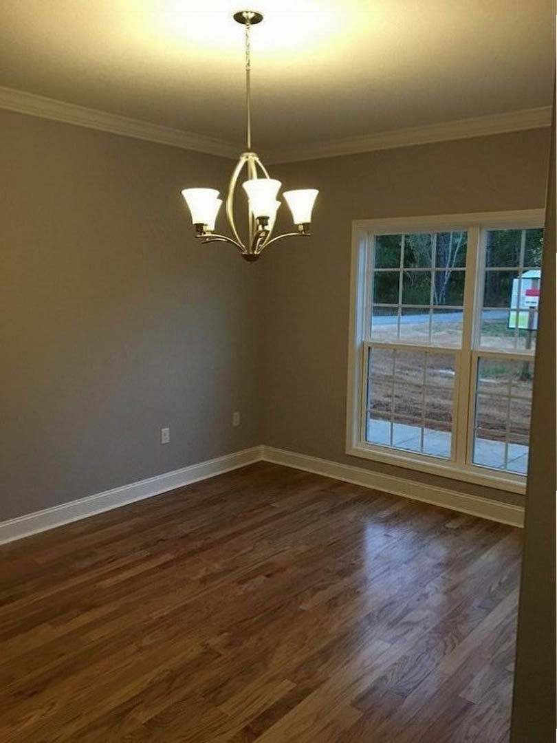 Chandelier with three lights hanging from a white plaster ceiling above hardwood flooring, multi-pane window letting in natural light, neutral walls.