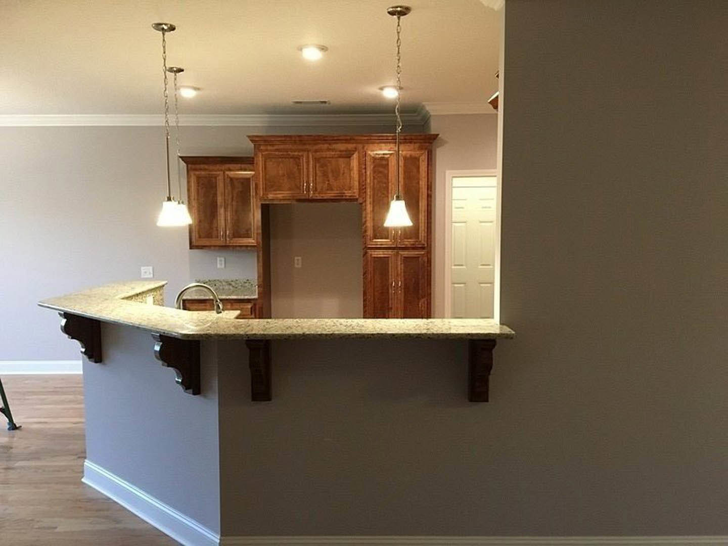 Open-concept kitchen featuring a bar with white cabinetry, quartz countertops, stainless steel sink, pendant bell-shaped light fixture, white door with illuminated light, and