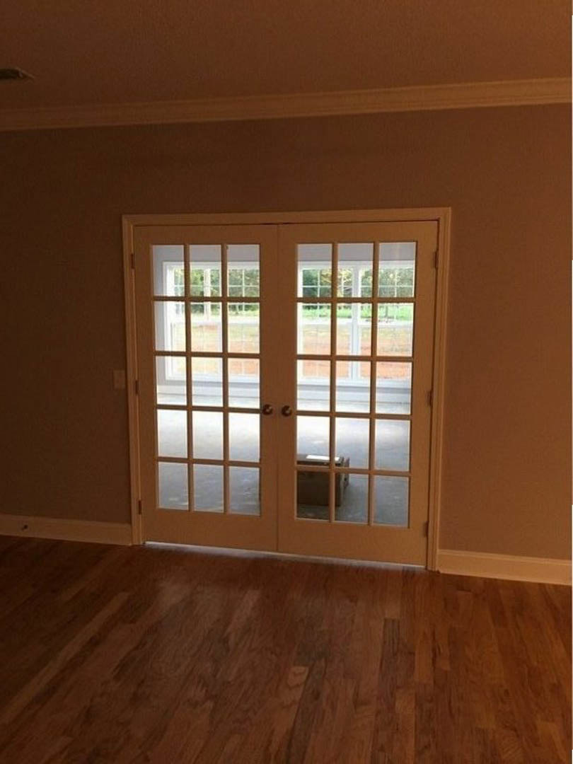 Double glass-paneled doors with white trim, wooden floor, window with white frame, neutral walls
