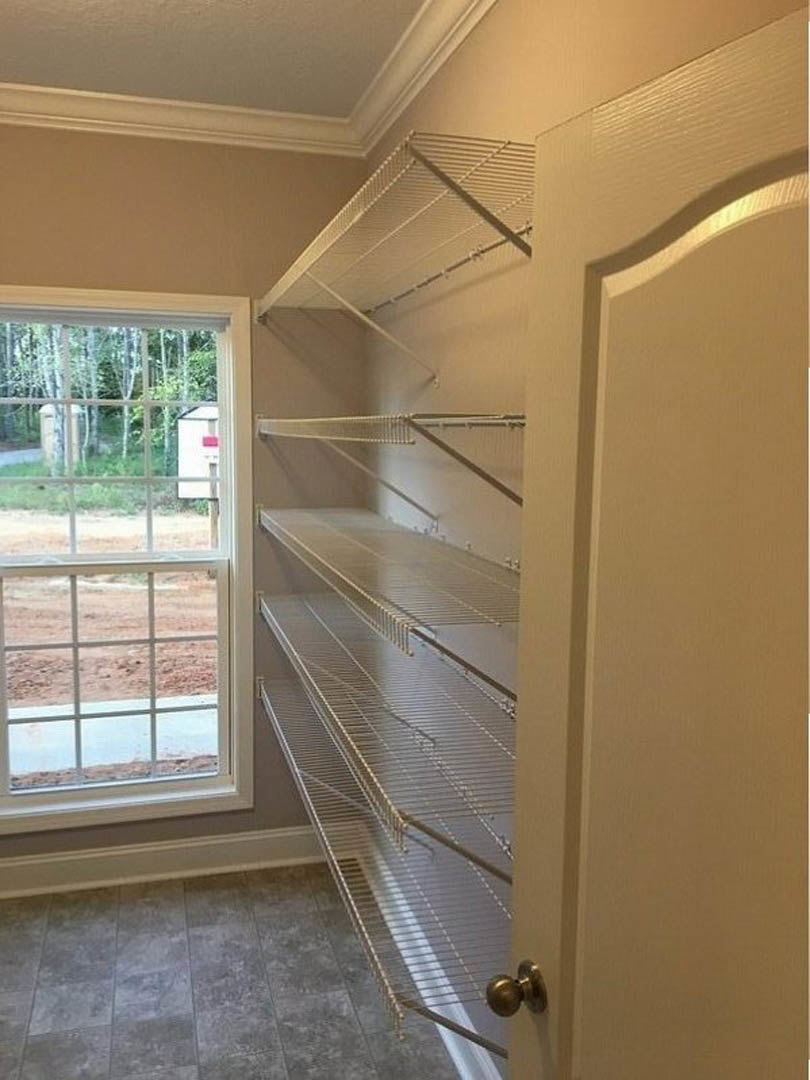 Built-in empty shelves along a white plaster wall, grey tile flooring, large window with outdoor view, close-up of a door knob