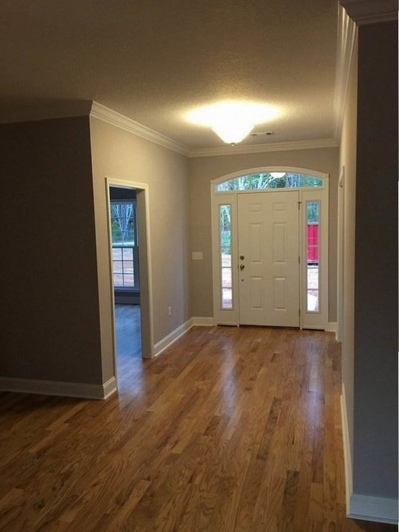 Hallway with hardwood flooring, white paneled door featuring glass panes and a silver doorknob, plaster walls, ceiling light fixture, and a window adjacent to the door