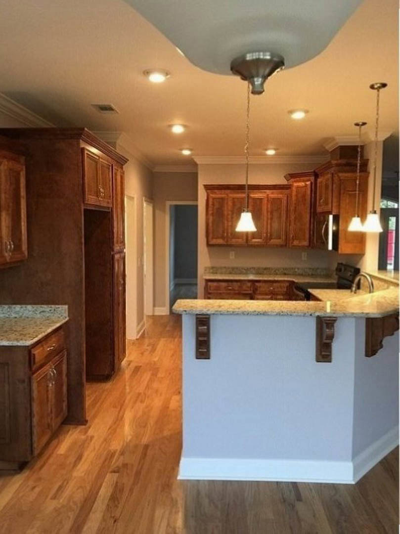 Kitchen with white countertop supported by brown brackets, brown wood paneling, ceiling fan, cabinetry, and sink; ceiling light and lamp shade visible.