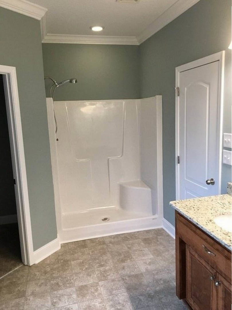 Bathroom with white tile shower featuring a step, granite countertop with undermount sink, tile flooring, and white cabinetry