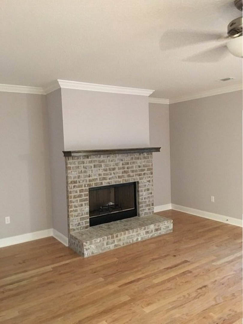 Stone fireplace with wood burning fire, wood flooring, white walls, and white molding in a cozy living room.