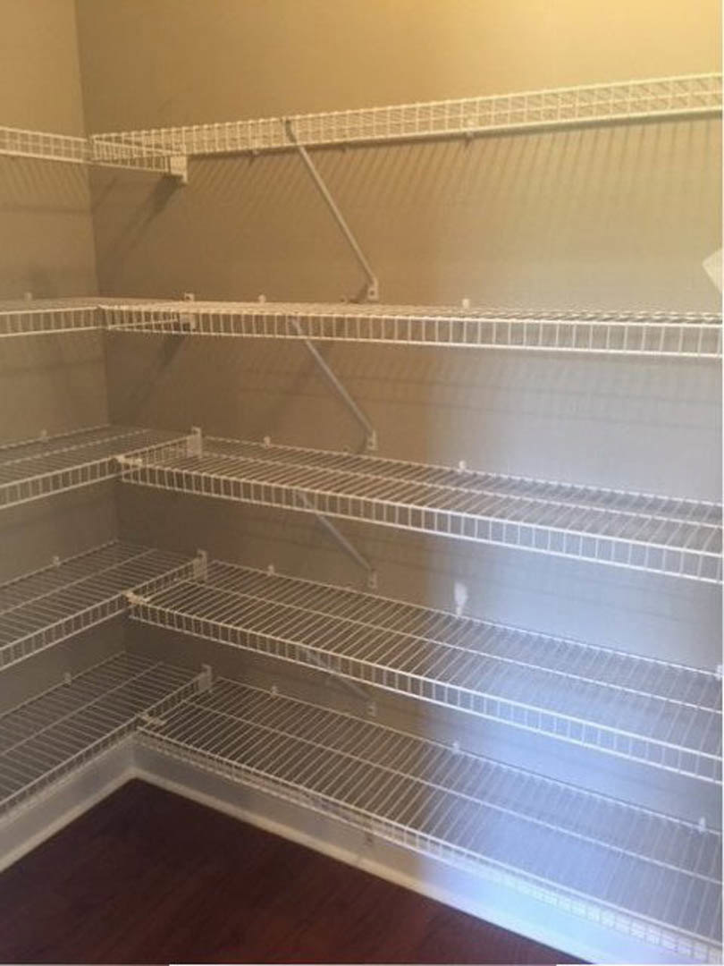 Empty closet with white metal shelves and hanging bar, wood floor with metal grate, white walls