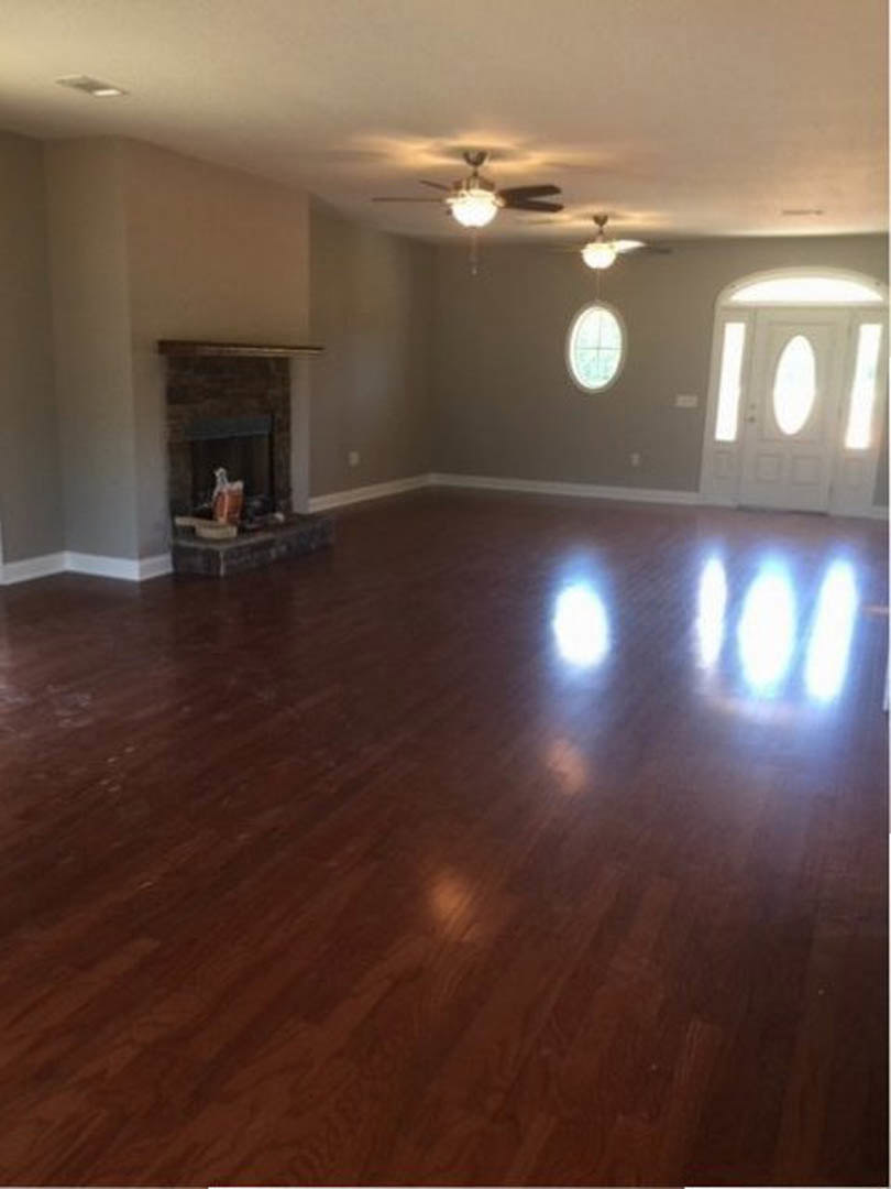 Living room with hardwood flooring, white fireplace, oval window in white door, sunlight streaming through window, light reflecting off floor