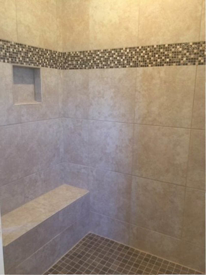 Walk-in shower with built-in bench, marble tile trim, and tiled floor, adjacent to tiled wall.