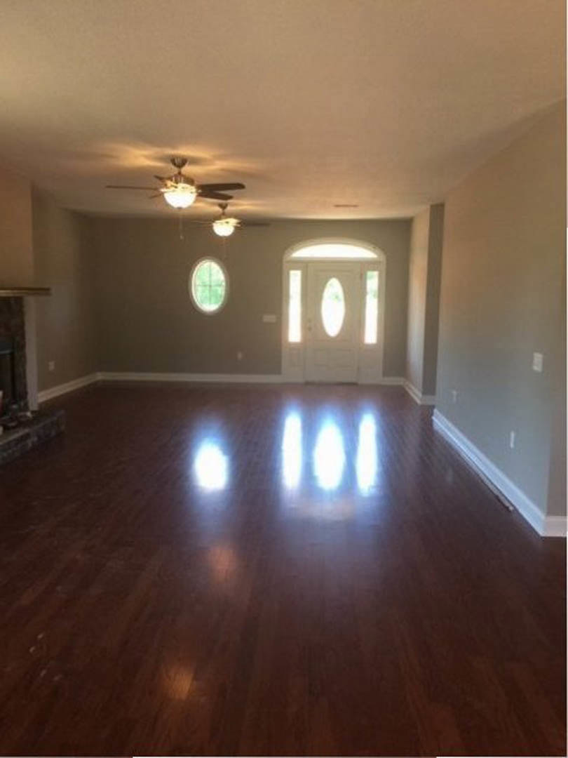 Wood flooring room with white walls, ceiling fan with light fixture, white door featuring glass window, and additional window allowing natural light.