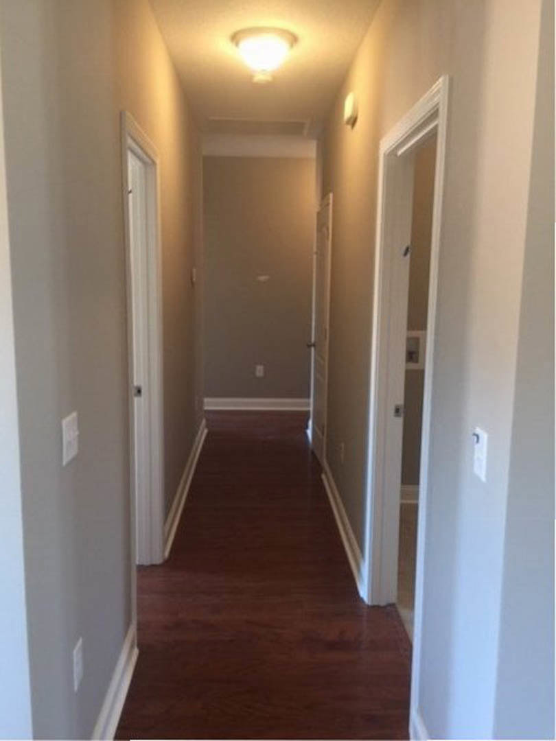Hallway with warm wood flooring, white walls, recessed ceiling light, multiple white doors and door frames, and a white pillar along the wall