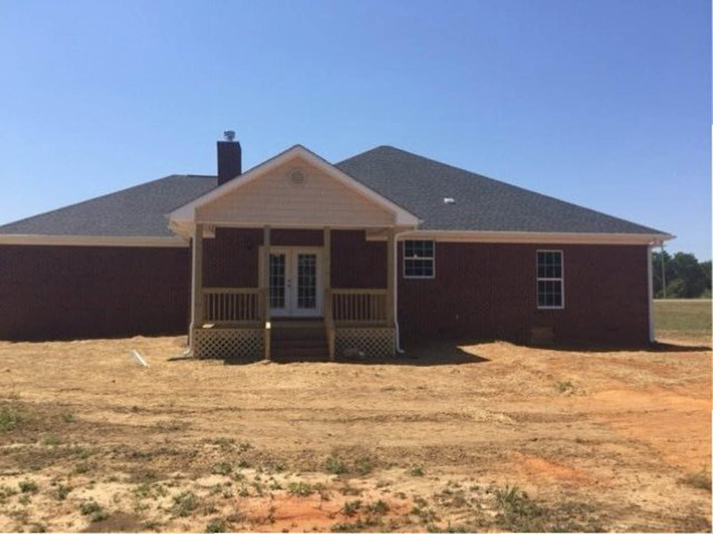 Front porch with white double doors and glass panes, white-framed window, dirt field with patches of grass in foreground, cottage-style exterior under open sky