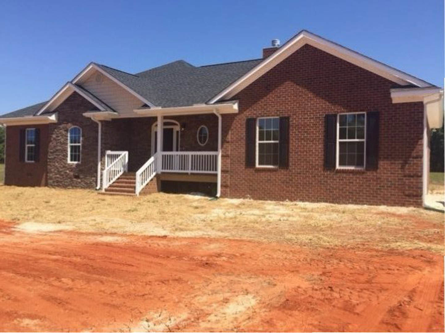 Brick house under construction with white porch railing, white-framed windows, dirt yard, and bird in background